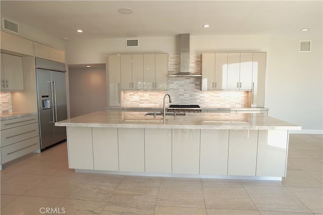 2615 Temple Hills Dr, Laguna Beach, CA 92651 - kitchen featuring wall chimney range hood, built in refrigerator, decorative backsplash, a center island with sink, and light stone counters