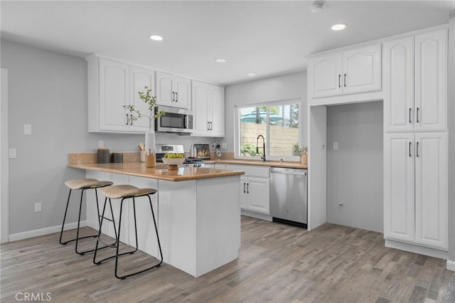 6831 Valinda Ave, Rancho Cucamonga, CA 91701 - kitchen featuring appliances with stainless steel finishes, light wood finished floors, a peninsula, white cabinetry, and recessed lighting