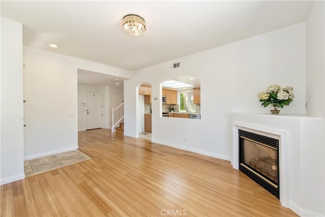 120 Rue Monet, Lake Forest, CA 92610 - unfurnished living room featuring a glass covered fireplace, light wood-style floors, stairway, arched walkways, and recessed lighting