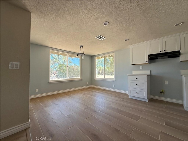 20219 Osseo Rd, Apple Valley, CA 92308 - kitchen featuring under cabinet range hood, a textured ceiling, wood finished floors, white cabinets, and decorative light fixtures