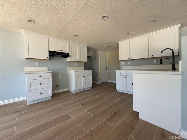 20219 Osseo Rd, Apple Valley, CA 92308 - kitchen with under cabinet range hood, wood finish floors, white cabinetry, a textured ceiling, and recessed lighting