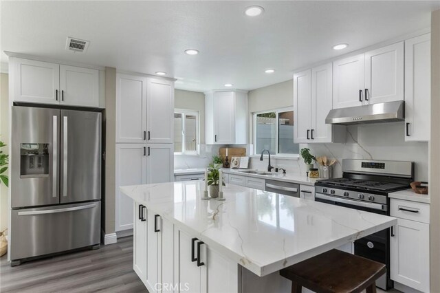 2306 255th St, Lomita, CA 90717 - kitchen with appliances with stainless steel finishes, under cabinet range hood, white cabinets, wood finished floors, and light stone counters