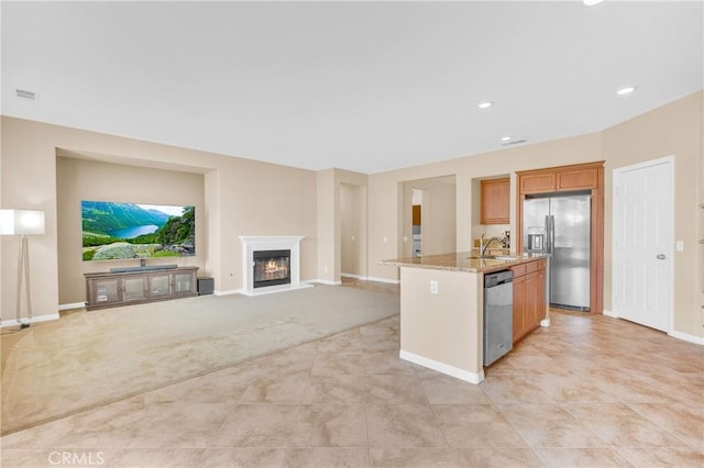 10850 Cameron Ct, Corona, CA 92883 - kitchen featuring stainless steel appliances, an island with sink, light stone counters, a glass covered fireplace, and light carpet