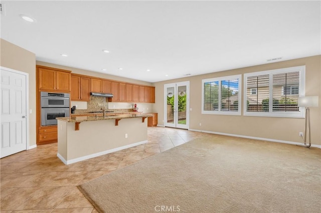 10850 Cameron Ct, Corona, CA 92883 - kitchen with appliances with stainless steel finishes, a kitchen breakfast bar, a kitchen island with sink, under cabinet range hood, and light tile patterned floors