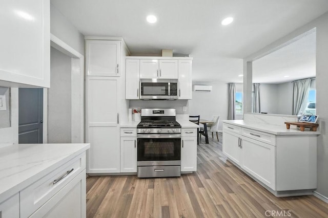 149 S Mistletoe Ave, San Jacinto, CA 92583 - kitchen with stainless steel appliances, white cabinetry, light wood-style flooring, a wall mounted AC, and light stone counters