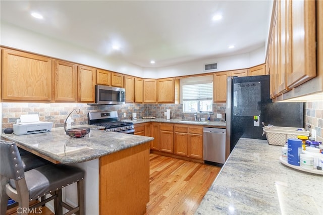 10838 Burnet Ave, San Fernando, CA 91345 - kitchen featuring stainless steel appliances, a peninsula, a kitchen bar, light wood finished floors, and tasteful backsplash