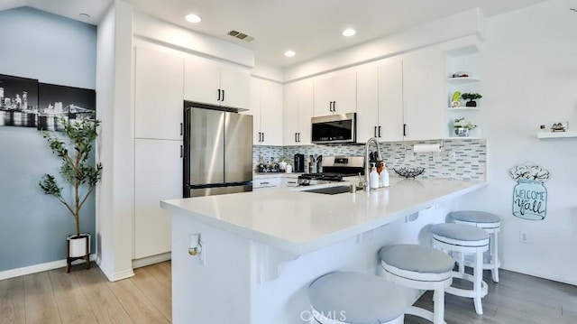 17554 Waterfall Ct, Fountain Valley, CA 92708 - kitchen featuring appliances with stainless steel finishes, a peninsula, light wood-style floors, a kitchen bar, and recessed lighting