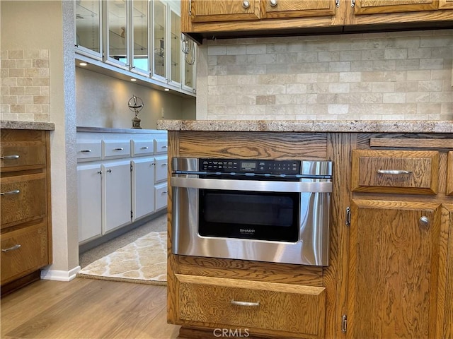 15381 Otomian Rd, Apple Valley, CA 92307 - kitchen featuring brown cabinets, light wood-style floors, backsplash, glass insert cabinets, and oven