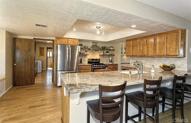 15381 Otomian Rd, Apple Valley, CA 92307 - kitchen featuring stainless steel appliances, brown cabinets, a peninsula, light wood finished floors, and a textured ceiling