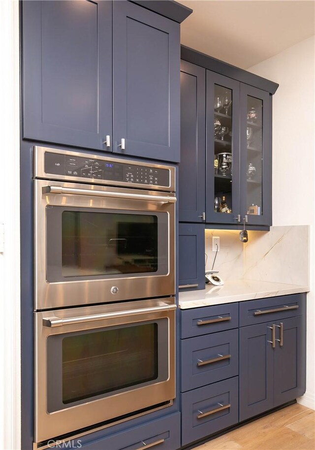 19680 Griffith Dr, Saugus, CA 91350 - kitchen with stainless steel double oven, glass insert cabinets, decorative backsplash, light wood-type flooring, and light stone countertops