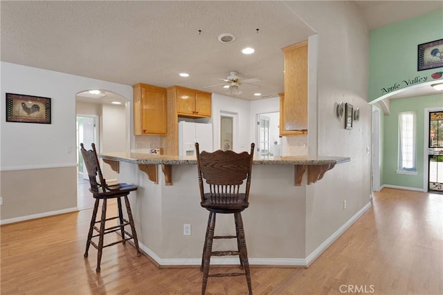 14908 Dakota Rd, Apple Valley, CA 92307 - kitchen featuring white refrigerator with ice dispenser, light wood-style floors, arched walkways, a ceiling fan, and a breakfast bar