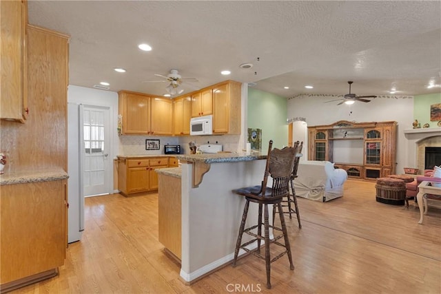 14908 Dakota Rd, Apple Valley, CA 92307 - kitchen with a ceiling fan, white microwave, light wood-style floors, a kitchen breakfast bar, and recessed lighting