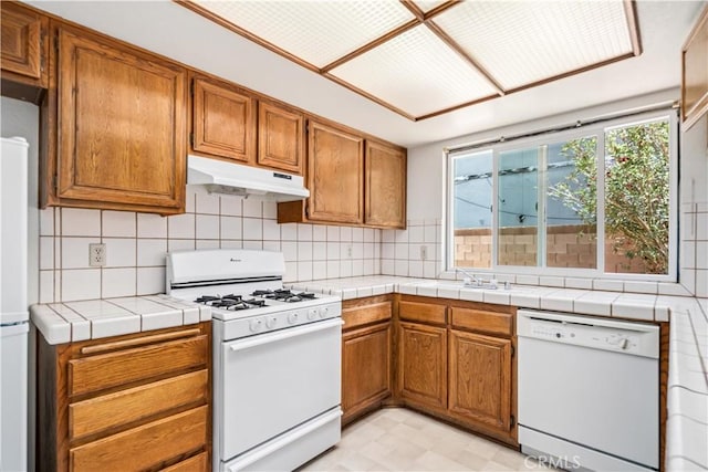 37224 Halfmoon Dr, Palmdale, CA 93550 - kitchen with white appliances, under cabinet range hood, brown cabinets, light flooring, and decorative backsplash