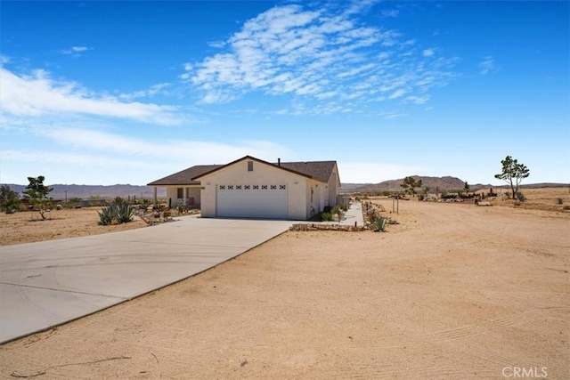 61975 La Brisa Dr, Joshua Tree, CA 92252 - single story home with driveway, an attached garage, a mountain view, and stucco siding