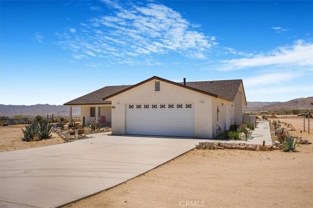 61975 La Brisa Dr, Joshua Tree, CA 92252 - ranch-style home with stucco siding, a mountain view, an attached garage, and driveway