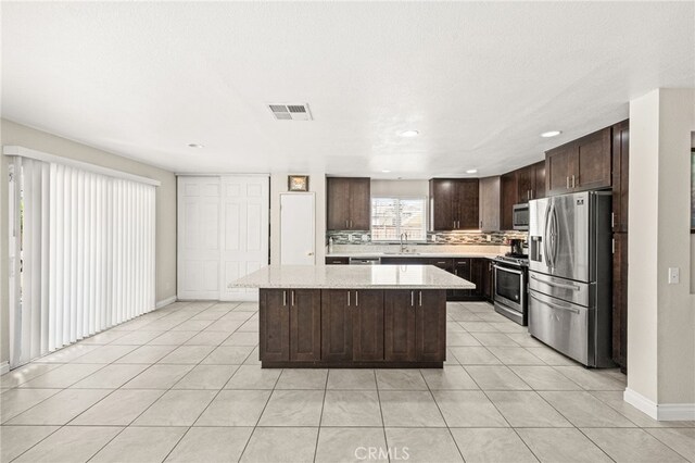 25969 Magnifica Ct, Moreno Valley, CA 92551 - kitchen featuring stainless steel appliances, dark brown cabinetry, a center island, light tile patterned flooring, and decorative backsplash