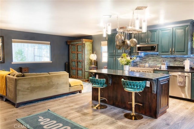 7695 Valle Ave, Atascadero, CA 93422 - kitchen featuring stainless steel appliances, light wood-style flooring, backsplash, dark countertops, and a breakfast bar