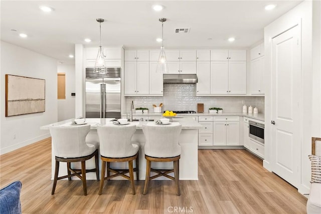 27636 S Evergreen Pl, San Pedro, CA 90732 - kitchen with stainless steel appliances, under cabinet range hood, light countertops, light wood finished floors, and decorative backsplash