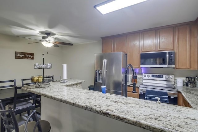 3454 Castle Glen Dr Unit 115, San Diego, CA 92123 - kitchen with stainless steel appliances, a ceiling fan, light stone counters, a kitchen breakfast bar, and brown cabinetry