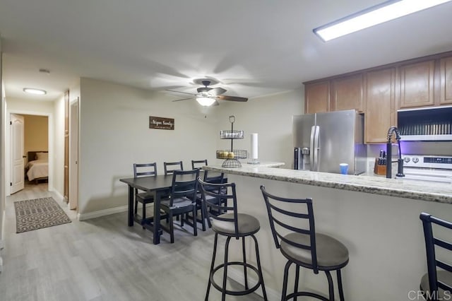 3454 Castle Glen Dr Unit 115, San Diego, CA 92123 - kitchen featuring stainless steel refrigerator with ice dispenser, a breakfast bar, ceiling fan, light wood-style floors, and light stone countertops