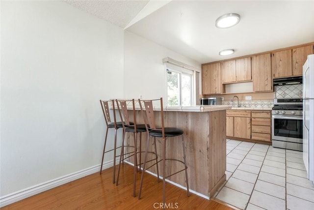 10919 Terecita Rd, Tujunga, CA 91042 - kitchen with stainless steel appliances, under cabinet range hood, a breakfast bar area, light countertops, and a peninsula