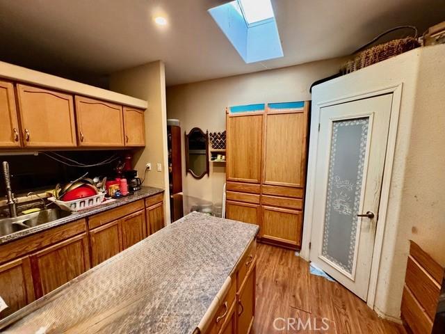 6475 105th St W, Rosamond, CA 93560 - kitchen with a skylight, brown cabinetry, wood finished floors, and light countertops