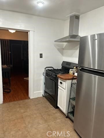 1388 N Lugo Ave, San Bernardino, CA 92404 - kitchen featuring freestanding refrigerator, black range with gas cooktop, wall chimney range hood, and white cabinets