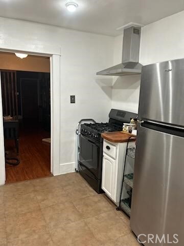 1388 N Lugo Ave, San Bernardino, CA 92404 - kitchen with freestanding refrigerator, black gas stove, wall chimney exhaust hood, and white cabinetry