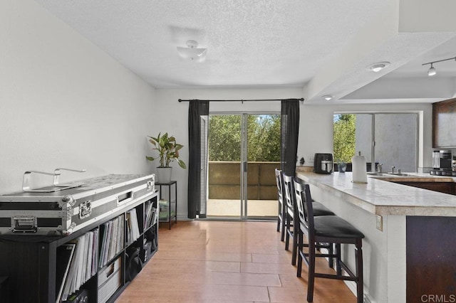 1317 Caminito Gabaldon Unit H, San Diego, CA 92108 - kitchen with a textured ceiling, a breakfast bar, light countertops, a peninsula, and light wood-style floors