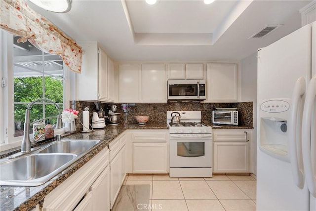 9909 Merced River Ave, Fountain Valley, CA 92708 - kitchen featuring white appliances, a tray ceiling, light tile patterned floors, decorative backsplash, and dark stone countertops