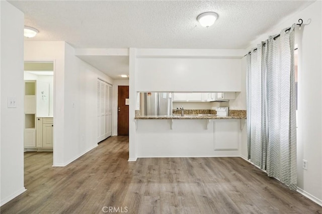 18900 Delaware St Unit 214, Huntington Beach, CA 92648 - kitchen with wood finished floors, a textured ceiling, freestanding refrigerator, a kitchen bar, and dark stone countertops