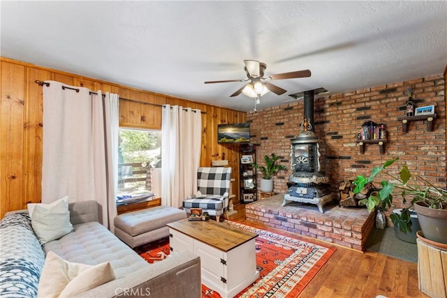 32135 W Dr, Running Springs, CA 92382 - living room featuring a wood stove, wood finished floors, ceiling fan, wood walls, and brick wall