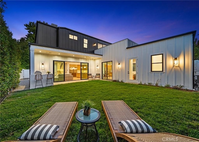 5945 Hesperia Ave, Encino, CA 91316 - back of house at dusk featuring board and batten siding, a lawn, and a patio