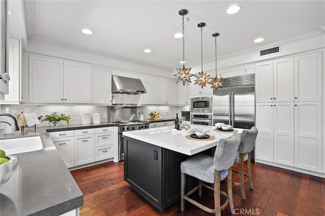 11 Heartwood Way, Aliso Viejo, CA 92656 - kitchen featuring wall chimney range hood, built in appliances, ornamental molding, a kitchen island, and white cabinets