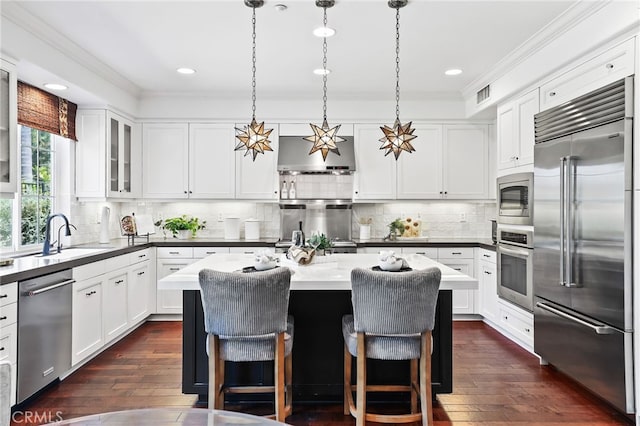 11 Heartwood Way, Aliso Viejo, CA 92656 - kitchen featuring built in appliances, ornamental molding, a kitchen island, white cabinetry, and wall chimney range hood