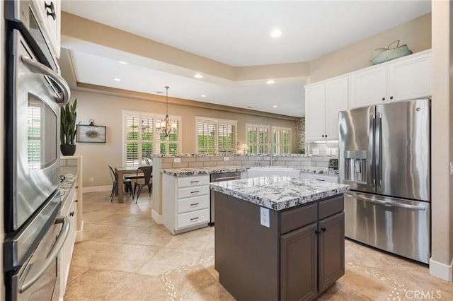 79787 Parkway Esplanade N, La Quinta, CA 92253 - kitchen with stainless steel appliances, a peninsula, white cabinetry, backsplash, and light stone countertops