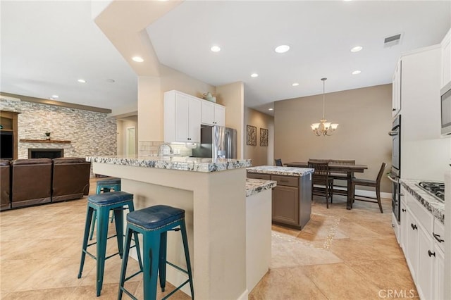 79787 Parkway Esplanade N, La Quinta, CA 92253 - kitchen featuring appliances with stainless steel finishes, a chandelier, a breakfast bar area, light stone counters, and recessed lighting