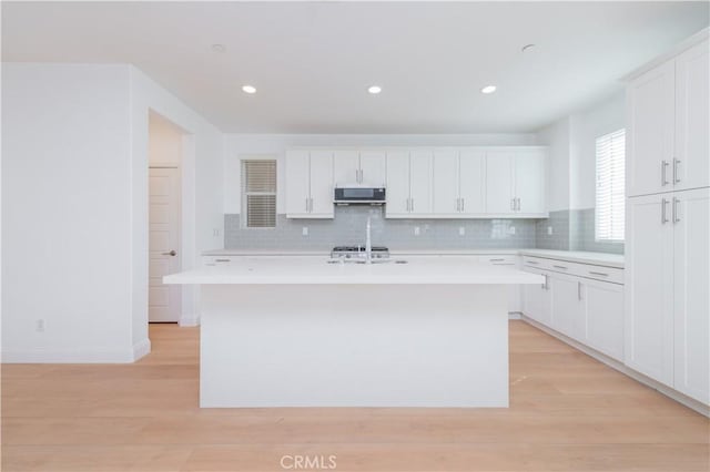 9570 Bluewater Pl, Rancho Cucamonga, CA 91730 - kitchen with light countertops, light wood-style floors, backsplash, a center island with sink, and white cabinets