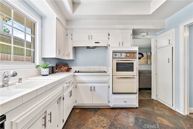 11752 Pine St, Los Alamitos, CA 90720 - kitchen featuring white double oven, dark stone finish floors, tile countertops, white cabinets, and under cabinet range hood
