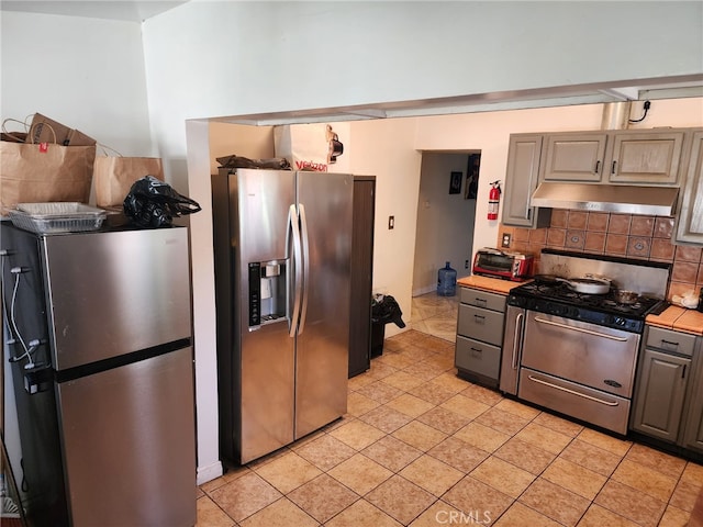 4312 Walton Ave, Los Angeles, CA 90037 - kitchen featuring appliances with stainless steel finishes, under cabinet range hood, tasteful backsplash, light countertops, and gray cabinetry