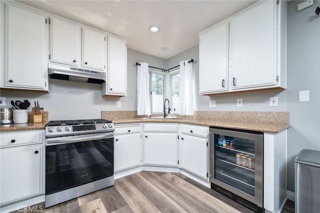 11718 Lucena Ave, Fontana, CA 92337 - kitchen featuring stainless steel range with gas stovetop, under cabinet range hood, wine cooler, light wood finished floors, and white cabinets