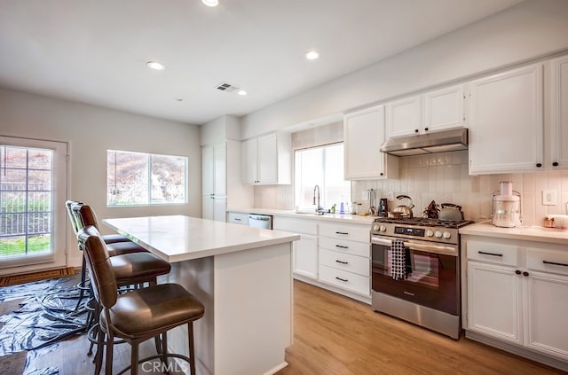 8550 Rolling Hills Dr, Corona, CA 92883 - kitchen with appliances with stainless steel finishes, under cabinet range hood, a kitchen bar, light countertops, and backsplash