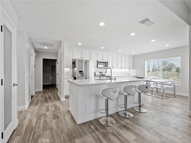 15679 Tuscola Rd, Apple Valley, CA 92307 - kitchen featuring stainless steel appliances, light countertops, light wood-style flooring, white cabinetry, and decorative backsplash