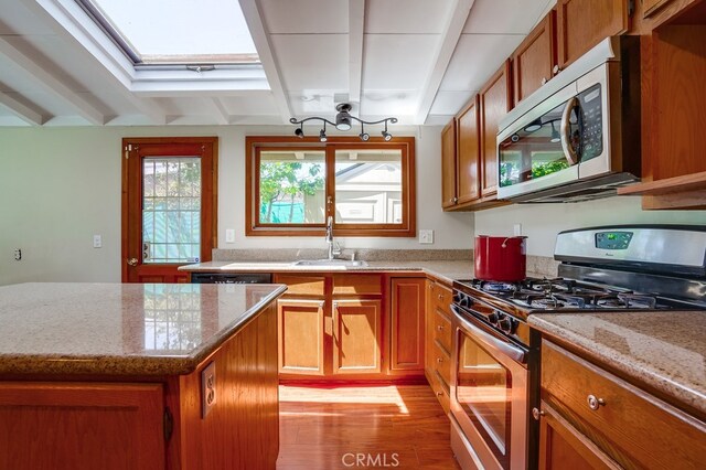 20606 Skouras Dr, Winnetka, CA 91306 - kitchen featuring stainless steel appliances, brown cabinets, a skylight, light wood finished floors, and beam ceiling