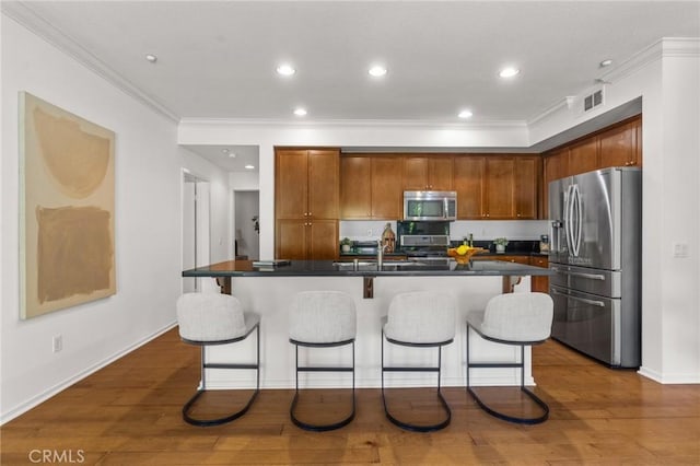 13028 Central Ave Unit 202, Hawthorne, CA 90250 - kitchen featuring stainless steel appliances, crown molding, a breakfast bar area, dark countertops, and a kitchen island with sink