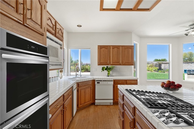31794 Corte Rosario, Temecula, CA 92592 - kitchen with appliances with stainless steel finishes, tile counters, light wood-style floors, a ceiling fan, and brown cabinetry