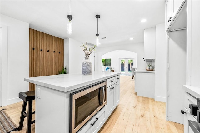 6816 E Driscoll St, Long Beach, CA 90815 - kitchen with stainless steel microwave, arched walkways, white cabinetry, light wood-style flooring, and hanging light fixtures