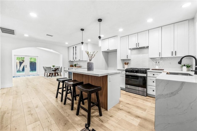 6816 E Driscoll St, Long Beach, CA 90815 - kitchen featuring stainless steel range with gas stovetop, arched walkways, white cabinets, tasteful backsplash, and light wood-type flooring