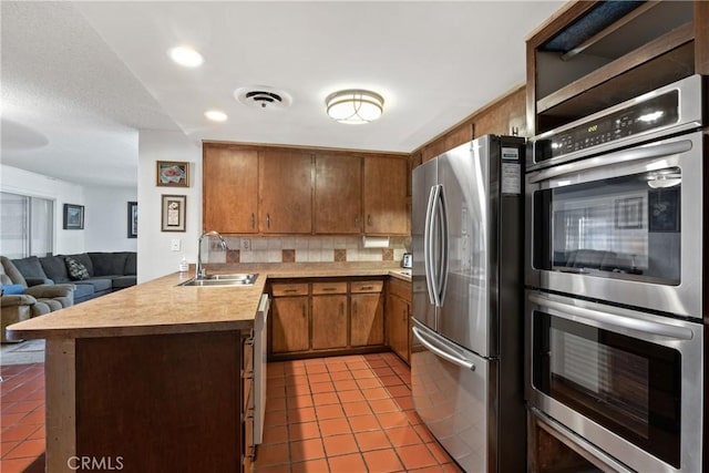 57795 El Dorado Dr, Yucca Valley, CA 92284 - kitchen featuring stainless steel appliances, tile patterned flooring, open floor plan, tasteful backsplash, and brown cabinets