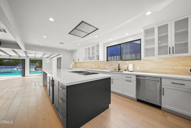 9518 Forbes Ave, Northridge, CA 91343 - kitchen with appliances with stainless steel finishes, white cabinetry, a kitchen island, decorative backsplash, and light wood finished floors
